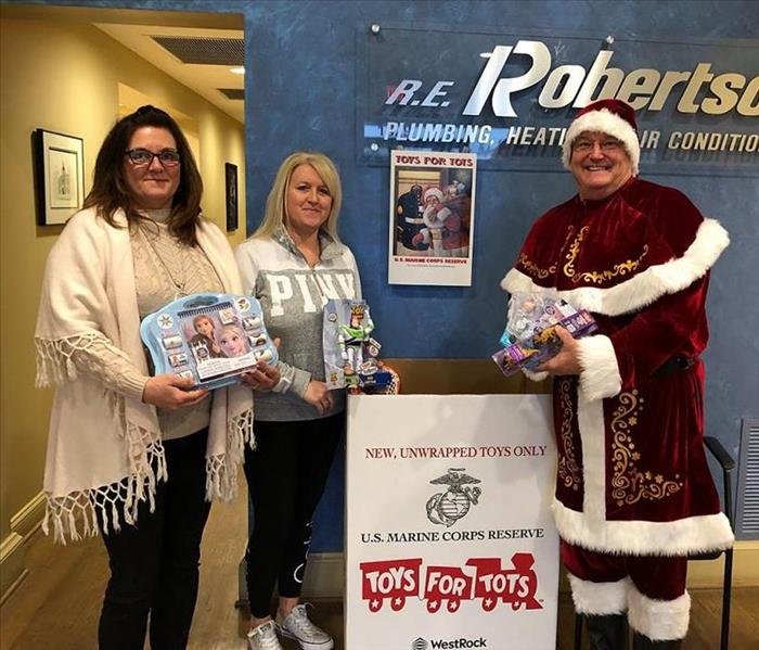 Santa and 2 ladies holding toys with Toys for Tots